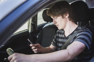 teen driver looking at his phone while driving car