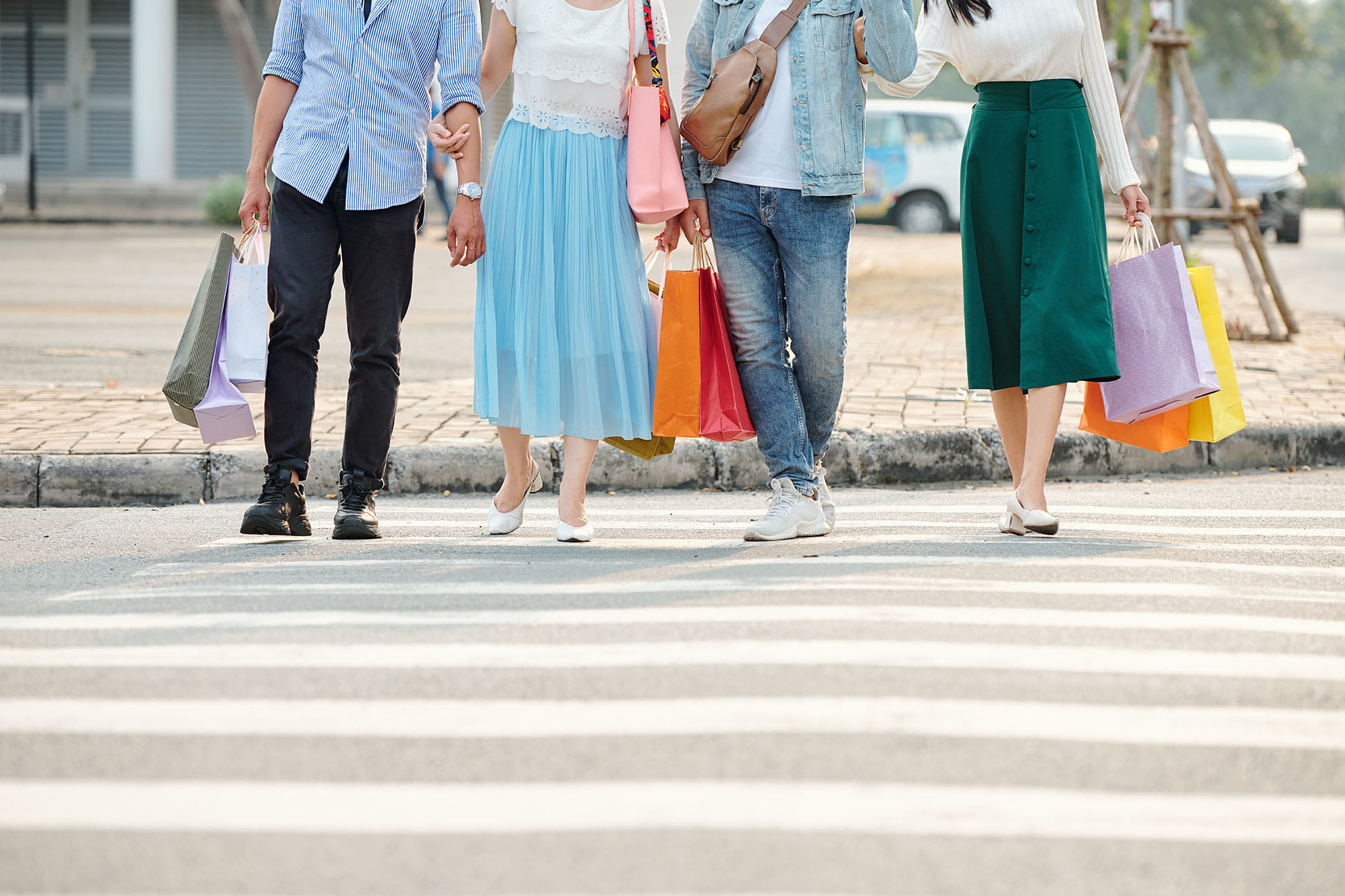 Cropped image of young people with shopping bags walking on pedestrian crosswalk