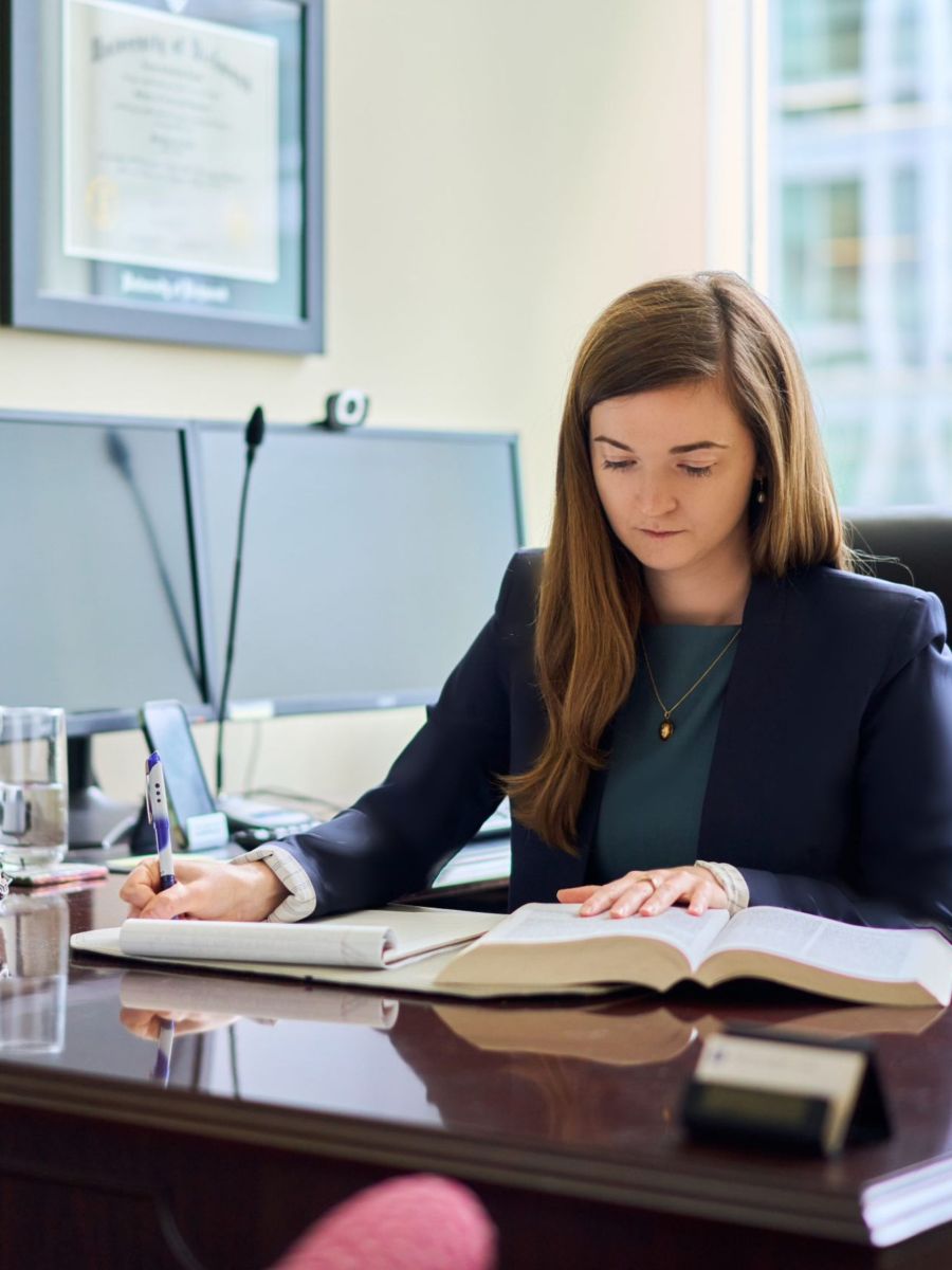 A dedicated female car accident lawyer from Regan Zambri Long is shown reviewing case documents in her Frederick, MD office. She sits at a wooden desk with legal books and notes, preparing detailed client casework related to auto accidents. Her work supports injury victims throughout Maryland, including those dealing with insurance claims, personal injury disputes, and court proceedings. To speak with a trusted Frederick car accident lawyer, contact Regan Zambri Long at 202-960-4596 for expert legal representation and results-driven advocacy.