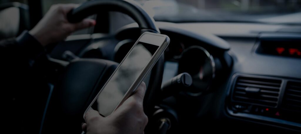 Inside view of a moving car where the driver is distracted, holding a smartphone in one hand while steering with the other. This image reflects dangerous behavior often linked to Lyft accidents in Washington, DC. Distracted driving remains a leading cause of rideshare collisions, especially in busy areas with traffic congestion. Law firms like Regan Zambri Long PLLC help injured passengers and third parties file claims after Lyft-related crashes. For legal help after a Lyft accident in the DC area, contact +1 (202) 937-3310.