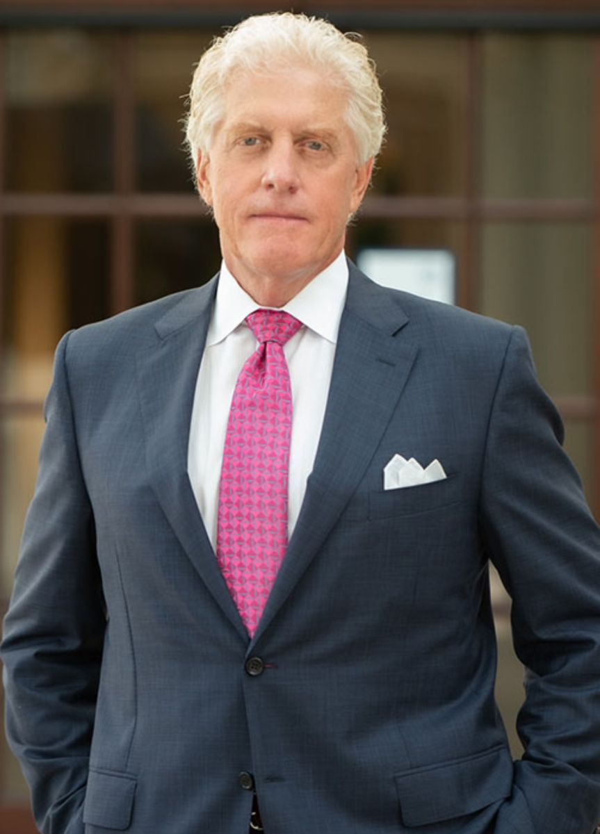 This professional portrait shows a male attorney in a dark blue suit and a patterned pink tie standing in front of a law office entrance in Fredericksburg, Virginia. Representing Regan Zambri Long PLLC, a law firm with a strong presence in pedestrian injury cases, the attorney is known for helping victims of serious crosswalk or road accidents in the Fredericksburg area. His confident expression and formal attire reflect a commitment to personal injury representation, specifically involving pedestrian collisions. Contact Regan Zambri Long at +1 (202) 937-3310 if you need a pedestrian accident lawyer serving clients throughout Fredericksburg and Northern Virginia.