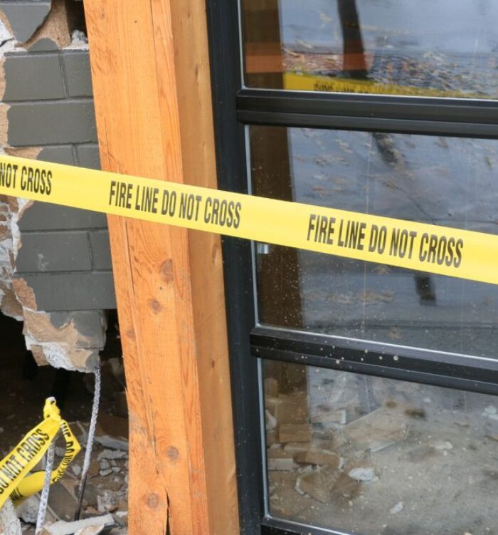 A commercial property in Baltimore, MD is cordoned off with yellow “Fire Line Do Not Cross” tape due to visible structural damage. A large hole in the brick wall and broken materials on the ground pose safety risks to visitors and employees. This image represents common premises liability claims involving unsafe property maintenance. Baltimore Premises Liability Lawyers at Regan Zambri Long PLLC handle injury claims resulting from hazardous conditions. For legal help in Baltimore, call (202) 937-3310.