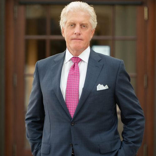 Patrick Regan, managing partner of Regan Zambri Long PLLC, is pictured standing outside a law office, wearing a navy blue suit, a bright pink tie, and a white pocket square. He is known for his leadership in personal injury and medical malpractice law in Washington, DC. The image reflects professionalism, legal authority, and over 25 years of legal service excellence.