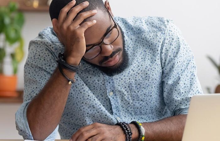 man holding his head at desk with computer